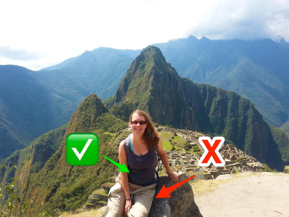 A woman in a gray tank and white pants sits on a rock in front of Machu Pichu.