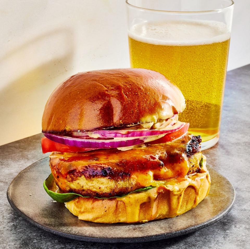 chicken burger topped with sauce, lettuce, sliced red onion, and tomato