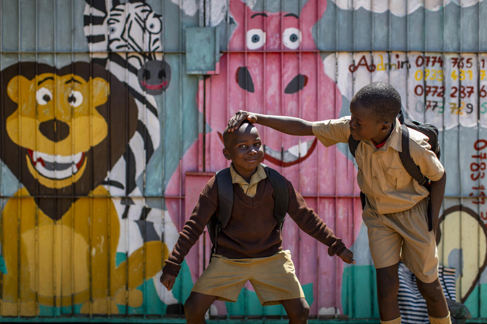 A schoolboy, right, jokes with his friend as his picture is taken, as they walk back home on the first day of the school term, in Kuwadzana, on the outskirts of the capital Harare, in Zimbabwe Tuesday, Sept. 10, 2019. Former president Robert Mugabe, who enjoyed strong backing from Zimbabwe's people after taking over in 1980 but whose support waned following decades of repression, economic mismanagement and allegations of election-rigging, is expected to be buried on Sunday, state media reported. (AP Photo/Ben Curtis)