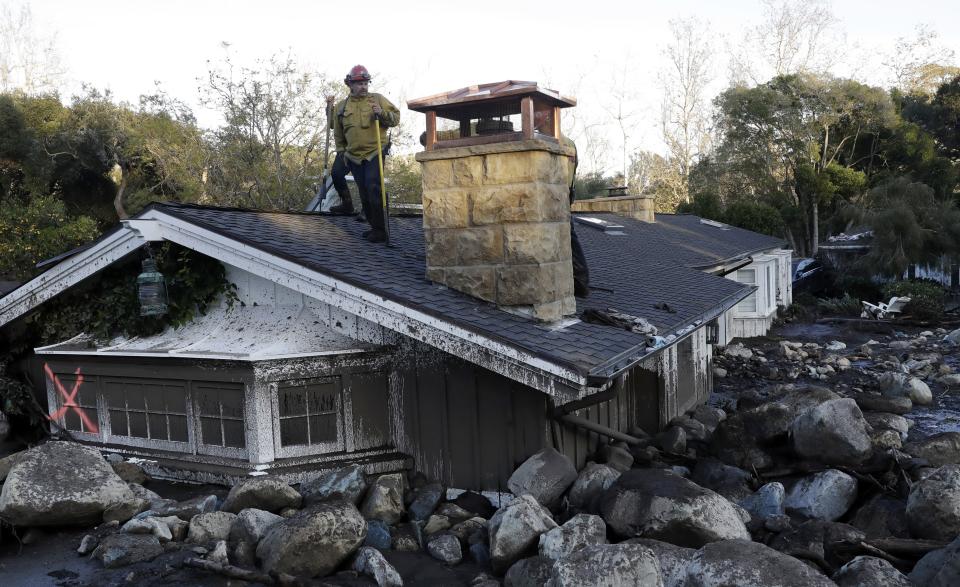 FILE - A firefighter stands on the roof of a house submerged in mud and rocks, Jan. 10, 2018, in Montecito, Calif. Experts say California has learned important lessons from the Montecito tragedy, and the state has more tools to pinpoint the hot spots and more basins and nets are in place to capture the falling debris before it hits homes. (AP Photo/Marcio Jose Sanchez, File)