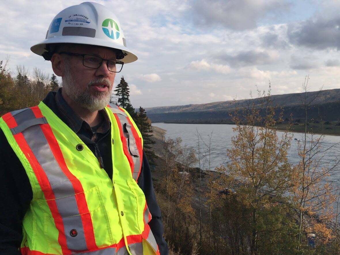 Bob Gammer stands on the banks of the Peace River above the construction site for the berm in September 2022. B.C. Hydro says the mound of rock and concrete will protect the town from erosion once Site C is operational. But it's also the reason the town needed a new water source.  (Kate Partridge/CBC News - image credit)