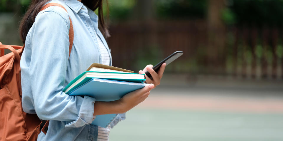 Student girl holding books and smartphone while walking in school campus background, education, back to school concept