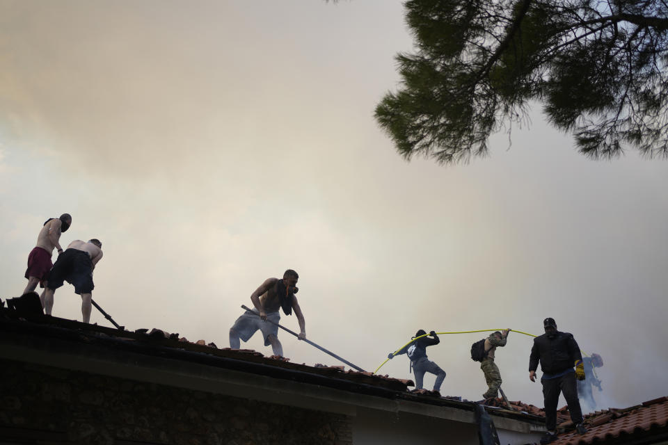 Men standing on the roof of Agia Paraskevi Christian Orthodox monastery try to control a wildfire in Acharnes, a suburb of northern Athens, Greece, Wednesday, Aug. 23, 2023. Water-dropping planes from several European countries joined hundreds of firefighters Wednesday battling wildfires raging for days across Greece that have left 20 people dead, while major blazes were also burning in Spain's Tenerife and in northwestern Turkey near the Greek border. (AP Photo/Thanassis Stavrakis)