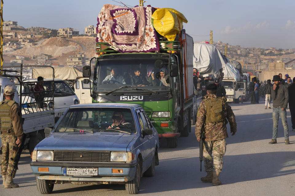 Lebanese soldiers pass next of trucks convoy that carry Syrian refugees and their belongings, at a gathering point where they prepare to cross the border back home to Syria, in the eastern Lebanese border town of Arsal, Lebanon, Wednesday, Oct. 26, 2022. Several hundred Syrian refugees boarded a convoy of trucks laden with mattresses, water and fuel tanks, bicycles – and, in one case, a goat – Wednesday morning in the remote Lebanese mountain town of Arsal in preparation to return back across the nearby border.(AP Photo/Hussein Malla)