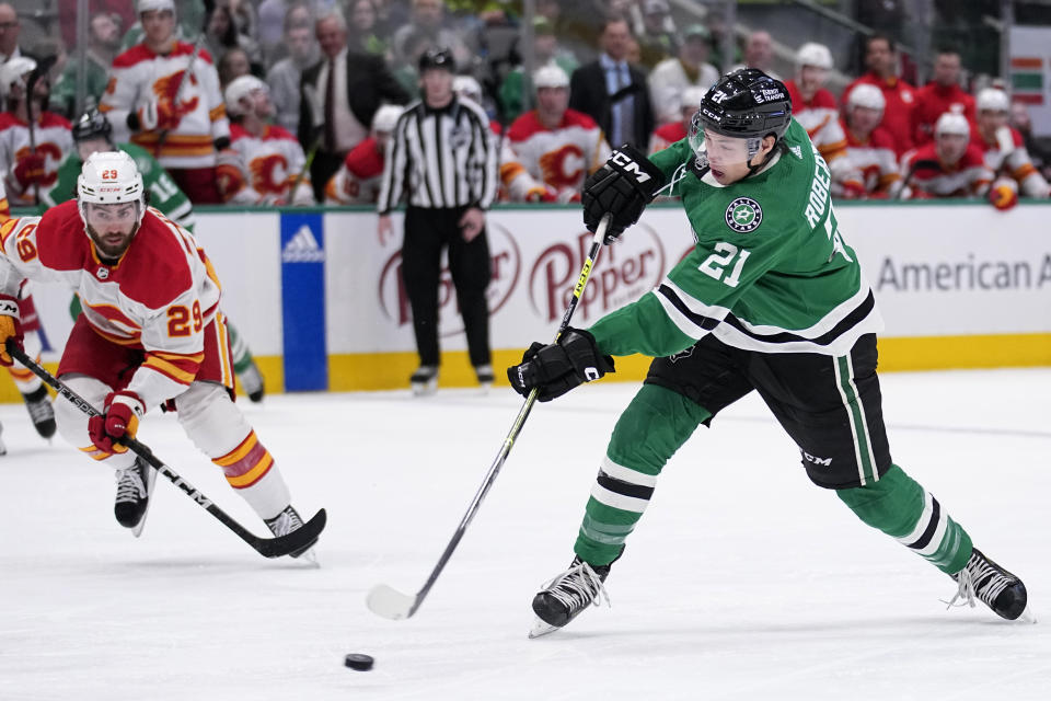 Dallas Stars left wing Jason Robertson (21) shoots as Calgary Flames' Dillon Dube (29) looks on in the first period of an NHL hockey game, Monday, March 6, 2023, in Dallas. (AP Photo/Tony Gutierrez)