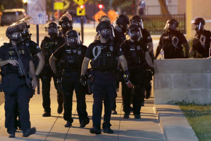 Police officers on a sidewalk deploy to confront protesters.