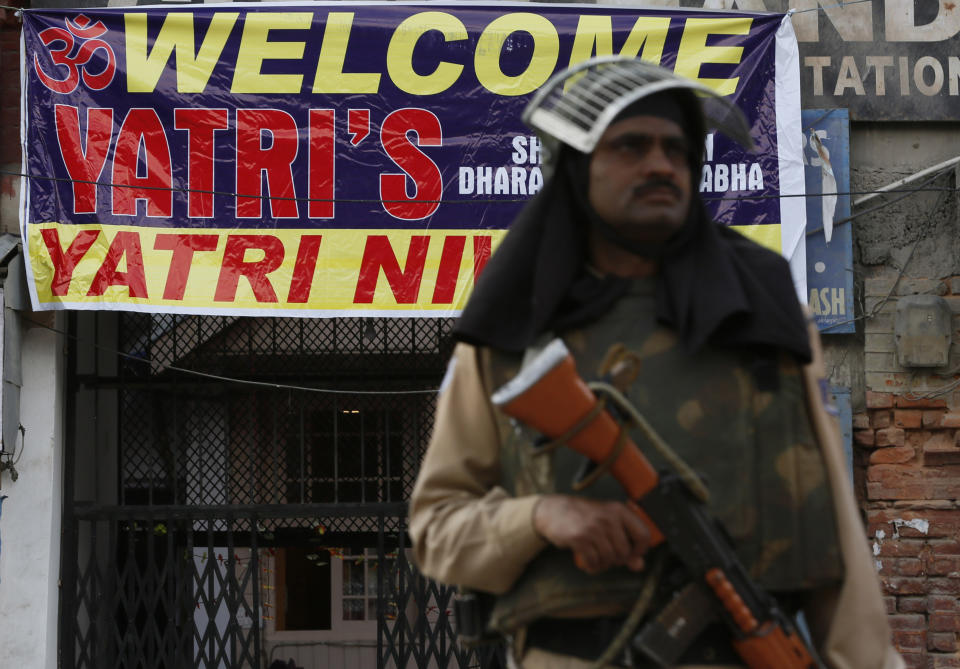 An Indian paramilitary soldier guards outside a Hindu temple next to a banner that welcomes pilgrims headed to the Amarnath cave shrine in Srinagar, Indian controlled Kashmir, Monday, July 1, 2019. Thousands of Hindu pilgrims began the arduous trek to an icy Himalayan cave in disputed Kashmir on Monday, with tens of thousands of Indian government forces guarding roads and mountain passes. (AP Photo/Mukhtar Khan)