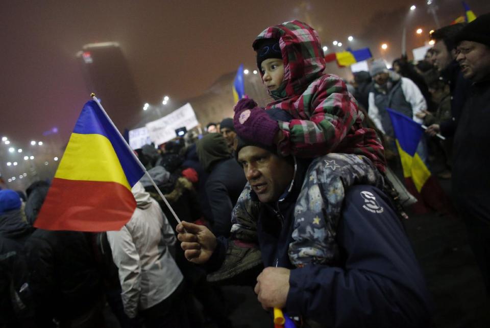 A man with a child waves a Romanian flag during a protest in Bucharest, Romania, Monday, Feb. 6, 2017. The leader of Romania's ruling center-left coalition said Monday the government won't resign following the biggest demonstrations since the end of communism against a measure that would ease up on corruption. (AP Photo/Darko Bandic)