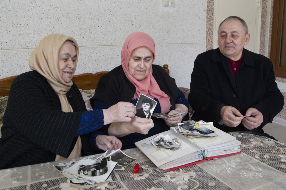 In this Sunday, March 17, 2019, photo, Zharadat Titiyeva, left, Khava Zakriyeva, center, and Yakub Titiyev look through the family pictures that feature their sibling, jailed activist Oyub Titiyev, at their family home in Kurchaloy, Chechnya, Russia. A court in Russia's Chechnya is due to issue its verdict Monday, March 18 in the case of the prominent rights activist. (AP Photo/Musa Sadulayev)