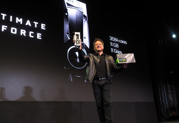 NVIDIA CEO Jensen Huang giving a presentation on a stage and holding up a graphics card in his hand.