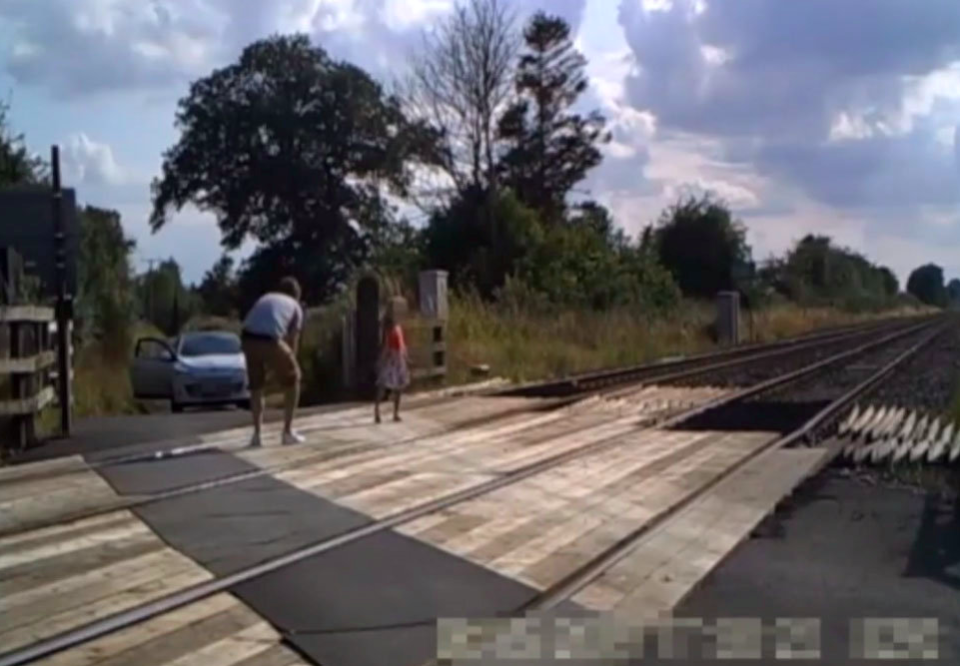 A car can be seen in the background with its doors open as the youngster adopts various poses on the level crossing. (SWNS)