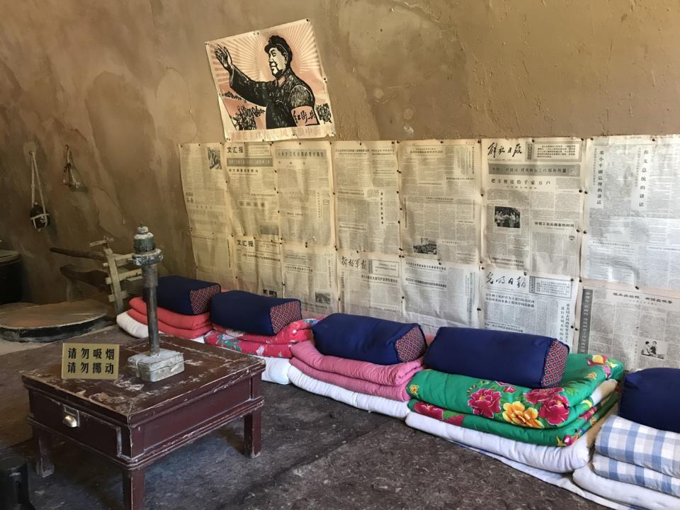 A poster of Mao and old newspapers hang on the wall in a cave.