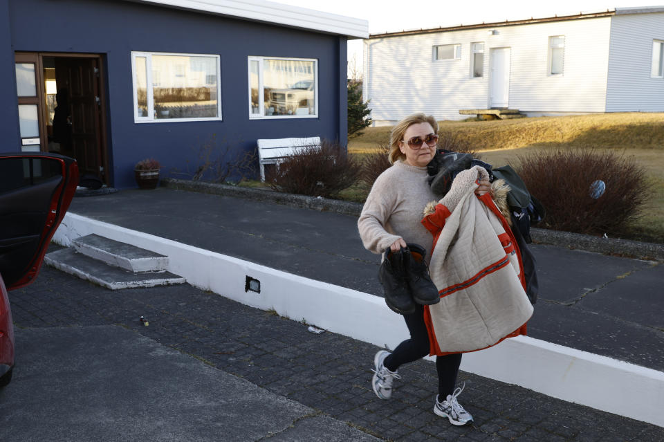 A woman carries belongings from a house.