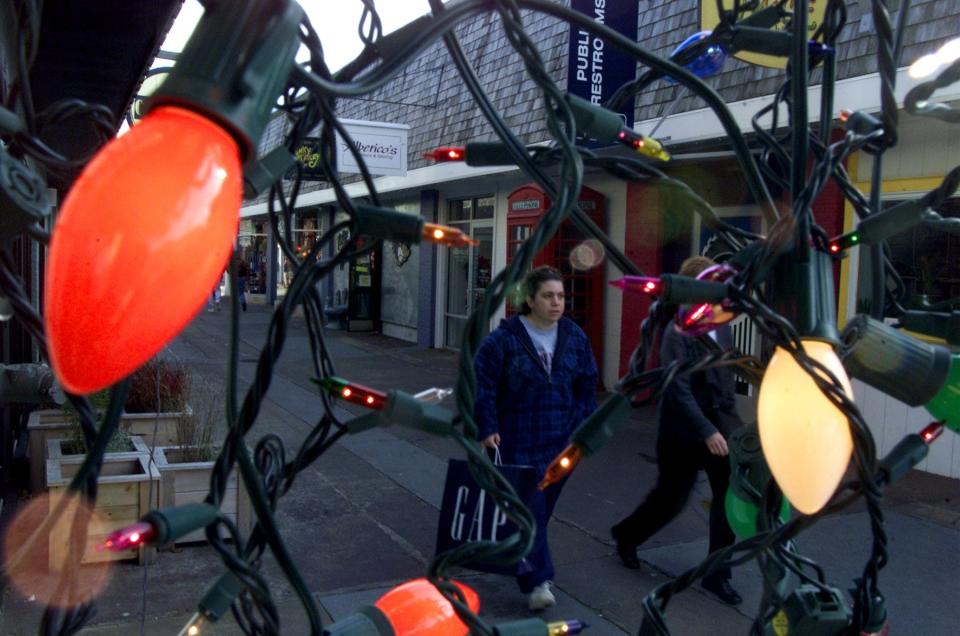 Holiday shoppers and browsers are framed by a jumble of Christmas lights strung along a walkway at Mashpee Commons where crowds have been turning out for the official start of the Christmas shopping season for more than 20 years.