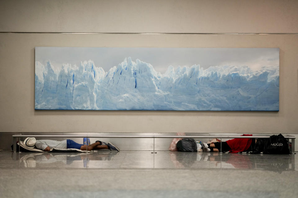 Homeless men sleep below a photo of the Perito Moreno Glacier at the Jorge Newbery international airport, commonly known as Aeroparque, in Buenos Aires, Argentina, Thursday, April 6, 2023. More than 100 homeless people sleep every night in a common area of the Aeroparque. (AP Photo/Natacha Pisarenko)