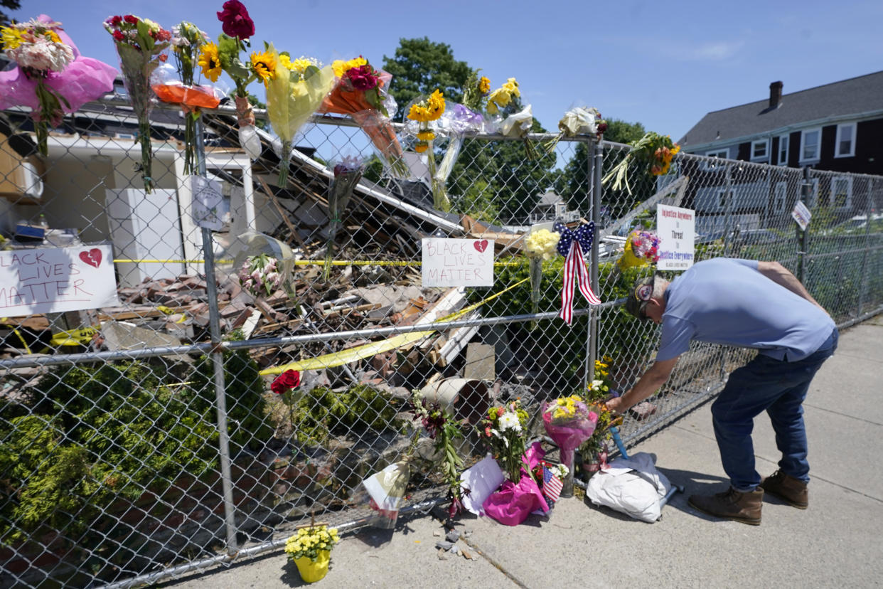 Herb Silk places flowers on a fence outside a building in Winthrop, Mass., on Monday, June 28, 2021, where an armed man crashed a hijacked truck, Saturday, June 26, 2021, then fatally shot two people before being killed by police. (AP Photo/Steven Senne)