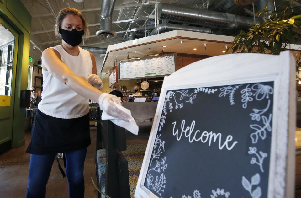 Laura Spencer, a recruiter at the corporate offices of the Fox Restaurant Concepts' Phoenix-based eateries, cleans off surfaces as she helps out at Flower Child restaurant as the restaurant is just one of the gradually opening full service dine-in establishments, expanding from their takeout option, to reopen as Arizona slowly relaxes restrictions due to the coronavirus, Monday, May 11, 2020, in Phoenix. (AP Photo/Ross D. Franklin)