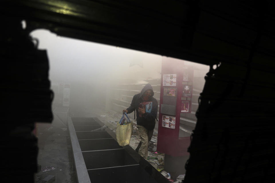 A man loots a small supermarket amid anti-government protests in Santiago, Chile, Monday, Oct. 28, 2019. Fresh protests and attacks on businesses erupted in Chile Monday despite President Sebastián Piñera's replacement of eight important Cabinet ministers with more centrist figures, and his attempts to assure the country that he had heard calls for greater equality and improved social services. (AP Photo/Esteban Felix)