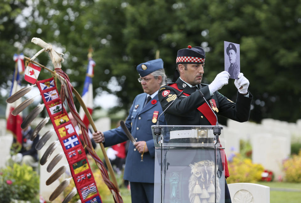 A member of the Canadian Armed Forces holds a photo of a Canadian World War II soldier during a ceremony at the Beny-sur-Mer Canadian War Cemetery in Reviers, Normandy, France, Wednesday, June 5, 2019. A ceremony was held on Wednesday for Canadians who fell on the beaches and in the bitter bridgehead battles of Normandy during World War II. (AP Photo/David Vincent)