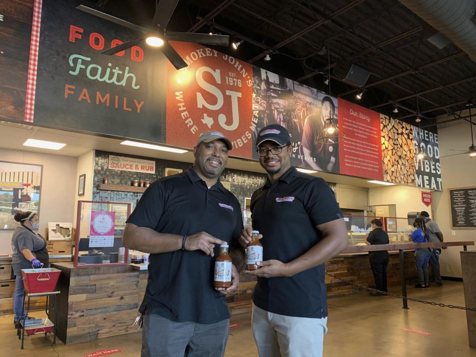 Juan Reeves, VP of Smokey John's BBQ, left, and his brother Brent Reeves, President of Smokey's John's BBQ, hold bottles of their famous barbecue sauce, which is available by mail order, at Smokey John's BBQ in Dallas on Dec. 10, 2020. (Jordyn Courtney/Smokey John's via AP)