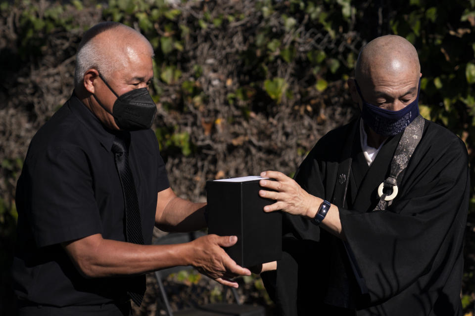 Clyde Matsumura, left, hands a small box containing the ashes of his grandfather, Giichi Matsumura, to Shumyo Kojima, a head priest of Zenshuji Buddhist Temple, during a memorial service at Woodlawn Cemetery in Santa Monica, Calif., Monday, Dec. 21, 2020. Giichi Matsumura, who died in the Sierra Nevada on a fishing trip while he was at the Japanese internment camp at Manzanar, was reburied in the same plot with his wife 75 years later after his remains were unearthed from a mountainside grave. (AP Photo/Jae C. Hong)