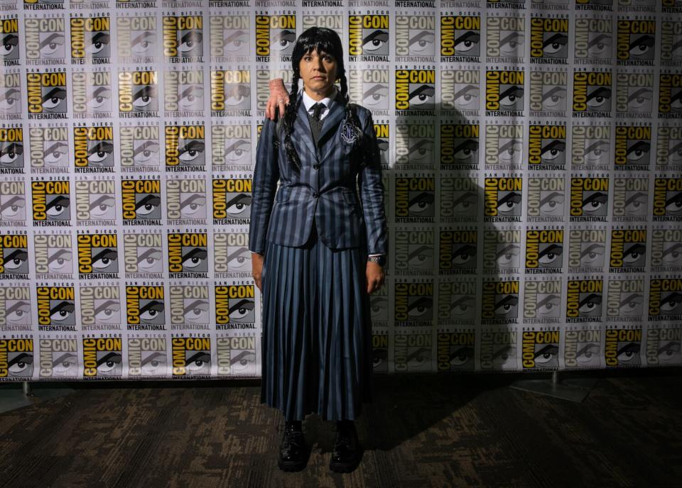 A cosplayer dressed as Wednesday Addams with Thing on her shoulder.