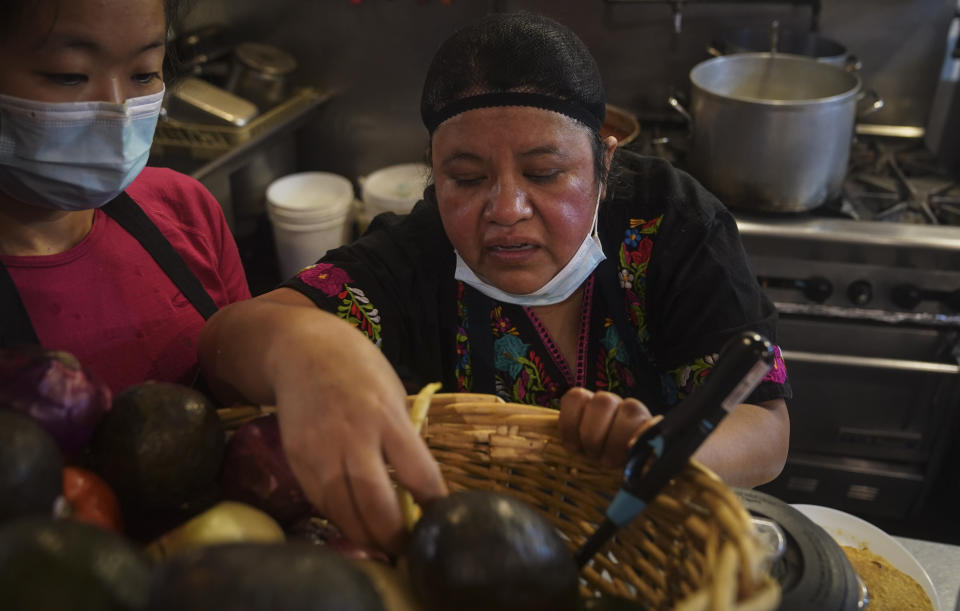 Natalia Méndez, right, goes through a basket of ingredients, as she prepare meals in the kitchen of La Morada, an award winning Mexican restaurant she co-owns with her family in South Bronx, Wednesday Oct. 28, 2020, in New York. After recovering from COVID-19 symptoms, the family raised funds to reopen the restaurant, which they also turned into a soup kitchen serving 650 meals daily. (AP Photo/Bebeto Matthews)