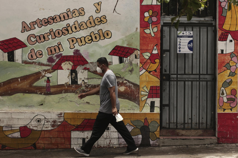 A pedestrian walks past a sign offering tips on safe social distancing and preventive measure to help curb the spread of the new coronavirus, in Santa Ana, El Salvador, Saturday, Aug. 22, 2020. After navigating legal snags and rigorous checks requiring they show they're in danger in Central America, refugees who were approved to come to the U.S. have faced more delays as the pandemic grounded flights, canceled final interviews and closed clinics that conduct needed medical exams. (AP Photo/Salvador Melendez)