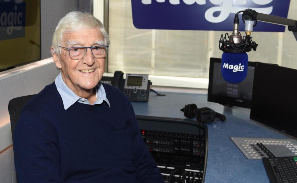 A man in a radio station studio wearing a blue sweater.