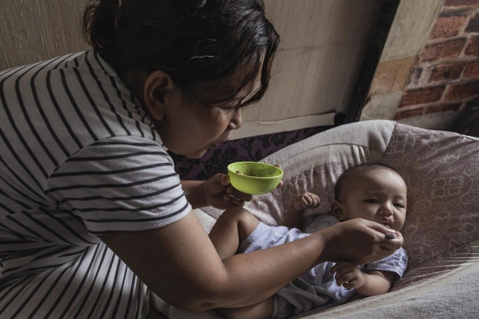 A woman holding a green bowl feeds an infant