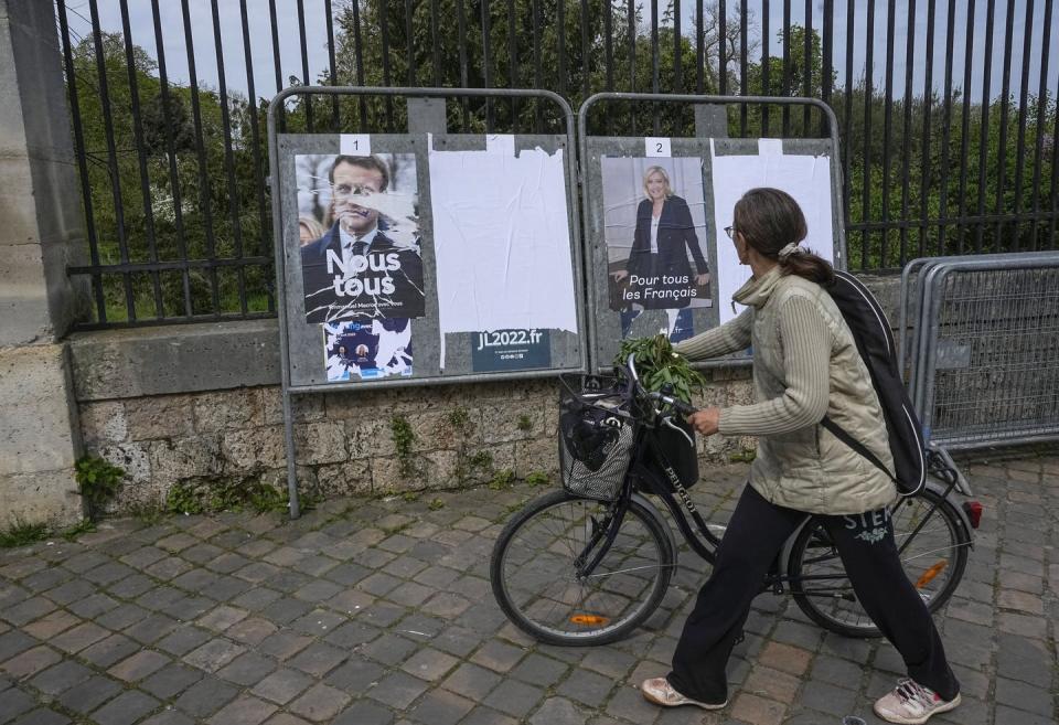 <span class="caption">A woman pushes her bike past campaign posters in Versailles ahead of the final vote.</span> <span class="attribution"><span class="source">Michael Euler/AP/AAP</span></span>