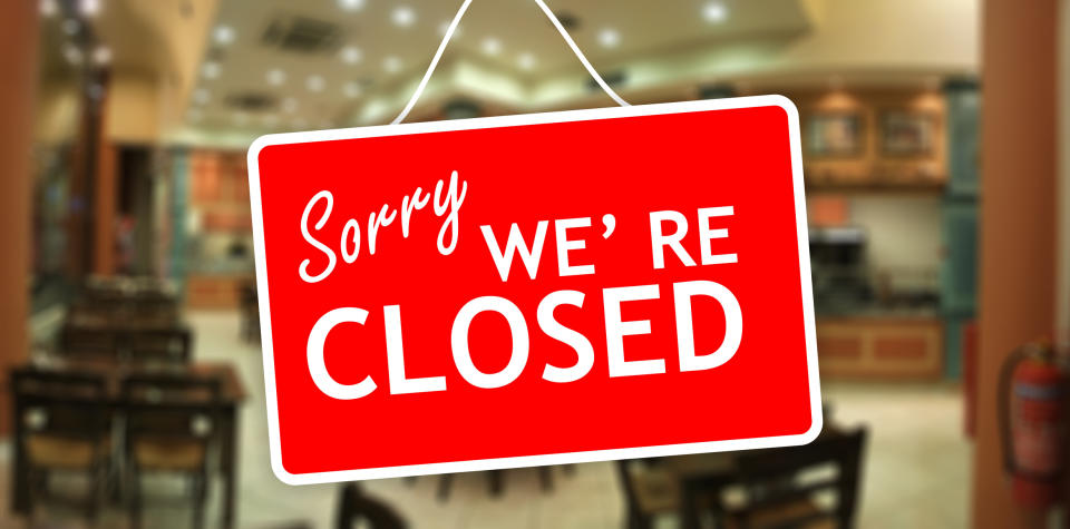 Sign reads "Sorry WE'RE CLOSED" hanging on a blurry background, possibly inside a shop