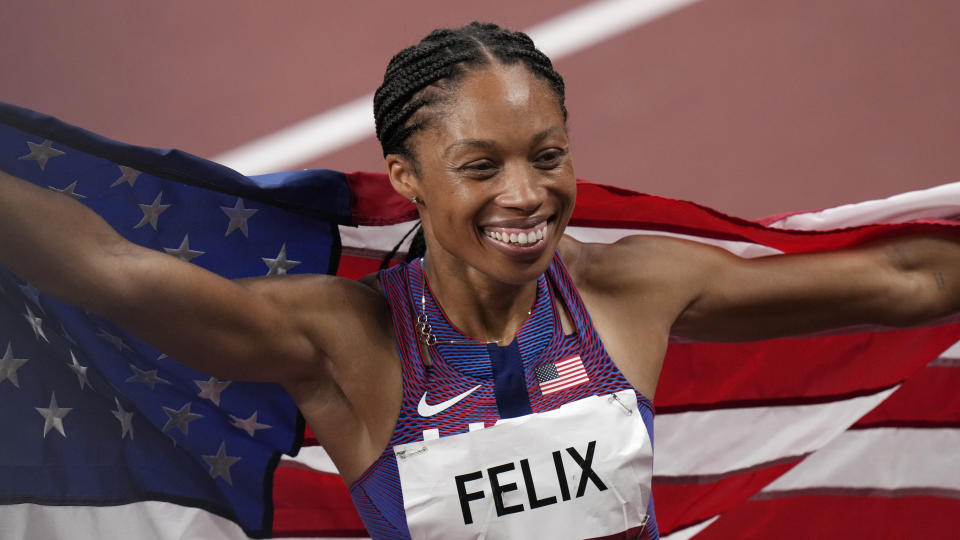 Allyson Felix smiles while holding an American flag on a track after winning a bronze medal.