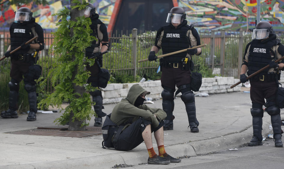 A lone protester sits down by state troopers as they block a street Friday, May 29, 2020 after another night of protests over the death of George Floyd who died in police custody Monday in Minneapolis. (AP Photo/Jim Mone)