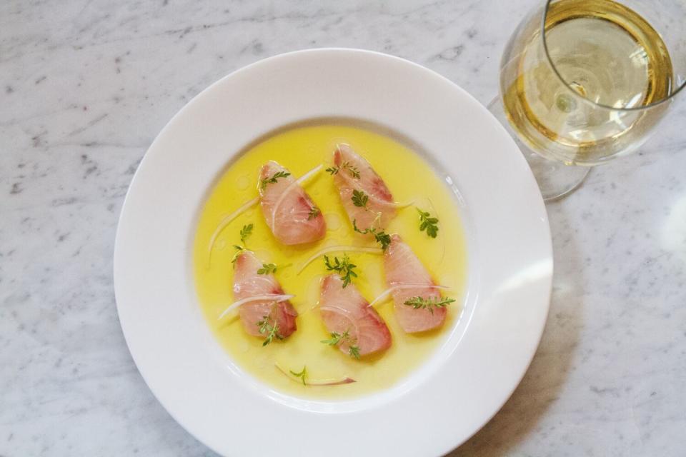 An overhead photo of kanpachi crudo in olive oil and calamansi vinegar on marble with a glass of white wine to the side