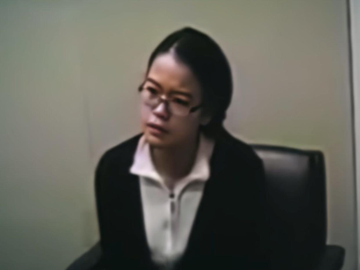 jennifer pan, a young woman with black hair and  glasses, sitting in a chair wearing a white shirt and black cardigan. the image quality is grainy and she looks inquisitve