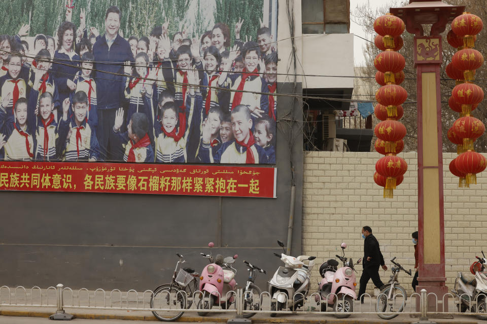 Residents walk past a propaganda board showing Chinese President Xi Jinping with local children and slogans calling for unity amongst the different ethnicities in Shule county in northwestern China's Xinjiang Uyghur Autonomous Region on March 20, 2021. Four years after Beijing's brutal crackdown on largely Muslim minorities native to Xinjiang, Chinese authorities are dialing back the region's high-tech police state and stepping up tourism. But even as a sense of normality returns, fear remains, hidden but pervasive. (AP Photo/Ng Han Guan)