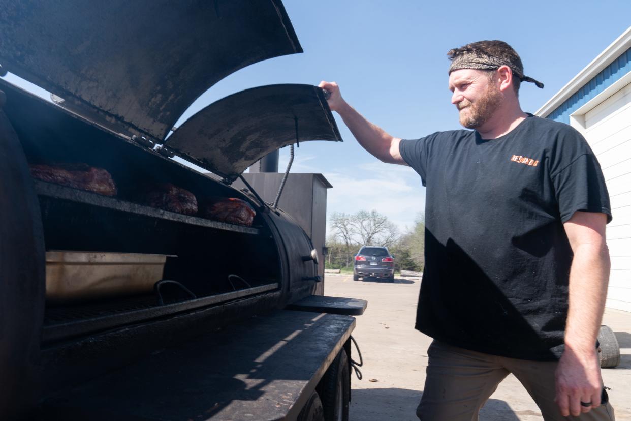 Tim Miller opens up his smoker outside of Happy Bassett Barrel House on Wednesday to show slabs of brisket he has smoking. Miller, owner of Beyond Q BBQ, finessed his smoking skills from his time in the U.S. Navy cooking for sailors on the open ocean.