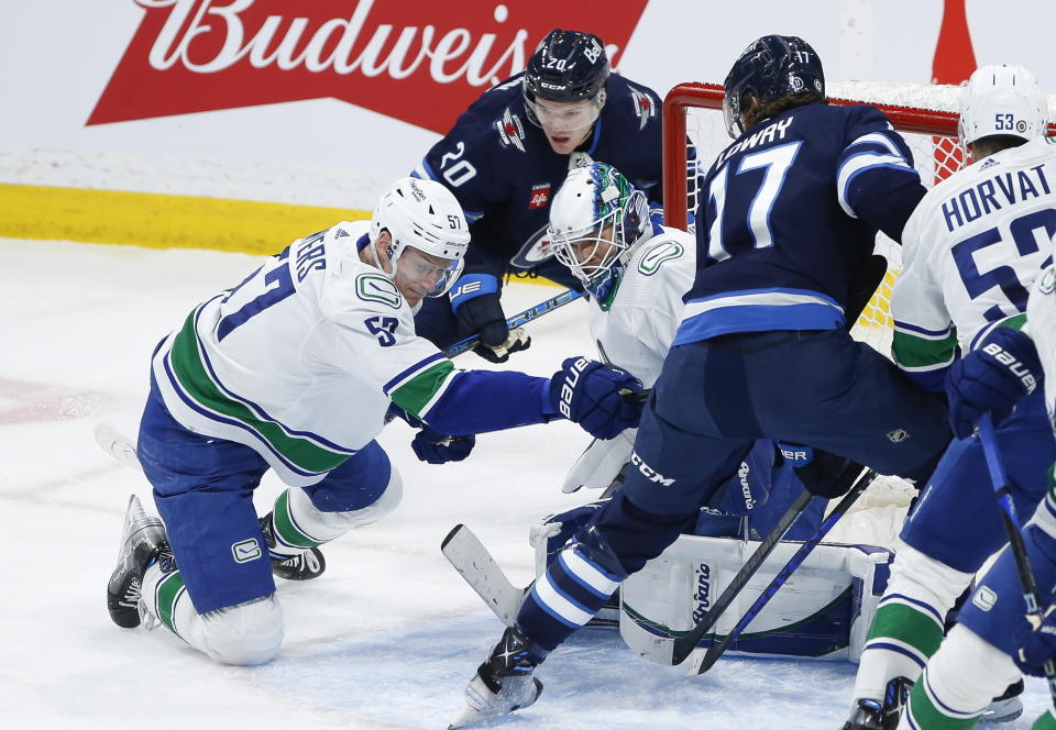Vancouver Canucks goaltender Collin Delia (60) saves against a shot by Winnipeg Jets' Adam Lowry (17) as Canucks' Tyler Myers (57) defends during second-period NHL hockey game action in Winnipeg, Manitoba, Thursday, Dec. 29, 2022. (John Woods/The Canadian Press via AP)
