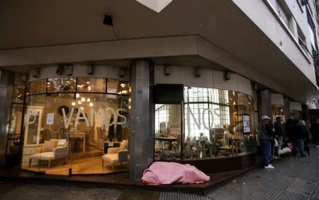 FILE PHOTO: A homeless person sleeps outside a shop with a graffiti on its windows that reads "we are leaving", one day after a national blackout, in Buenos Aires