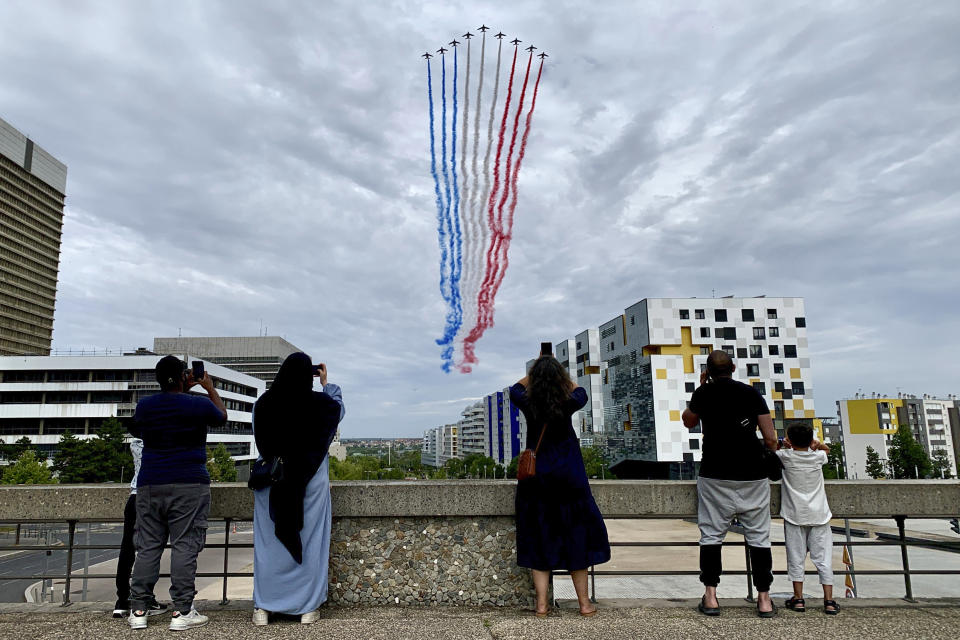 Residents watch jets from the Patrouille de France flying over Paris suburb Nanterre during the Bastille Day military parade Friday, July 14, 2023 in Nanterre. France celebrated its national holiday with whizzing warplanes and a grand Bastille Day parade in Paris — and with more than 100,000 police deployed around the country to prevent a new outbreak of unrest in underprivileged neighborhoods. (AP Photo/ Youcef Bounab)