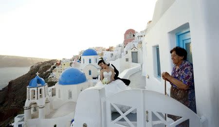 A resident looks on as as a couple have their wedding picture taken on the Greek island of Santorini, Greece, July 2, 2015. REUTERS/Cathal McNaughton/Files