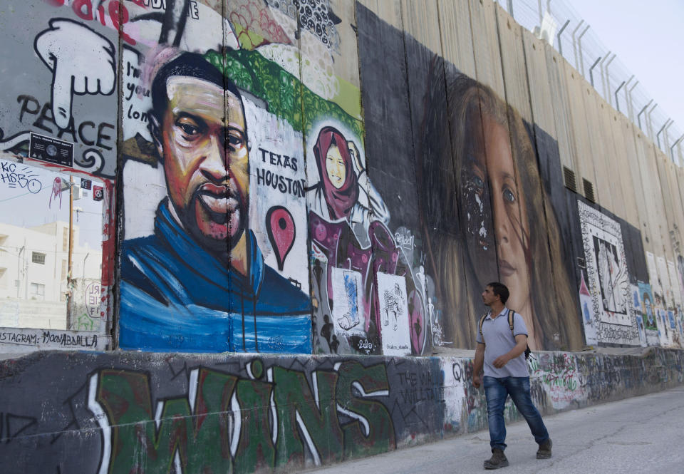 FILE- A Palestinian man walks past a mural that depicts George Floyd, a black American who died after being restrained by police officers in Minneapolis, at the Israeli separation wall in the West Bank city of Bethlehem, Monday, June 8, 2020. A growing number of Black Americans see the struggle of Palestinians reflected in their own fights for freedom and civil rights. In recent years, the rise of protest movements in the U.S. against police brutality in the U.S., where structural racism plagues nearly every facet of life, has connected Black and Palestinian activists under a common cause. But that kinship sometimes strains the alliance between Black and Jewish activists, which extends back several decades. (AP Photo/Nasser Nasser, File)