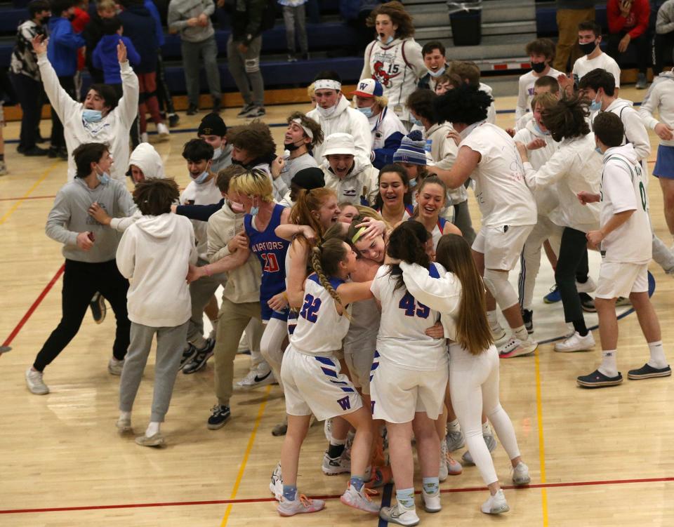 Winnacunnet's Abby Wilber is hugged by teammates as the Warrior student section storms the court after Wilber's half-court buzzer-beating shot beat Exeter, 42-40.