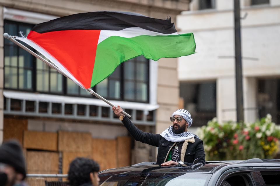 A participant of the "All Out for Gaza" rally and march on Saturday stands through the sunroof of a car waving a Palestinian flag at the front of the march that started at the Ohio Statehouse.