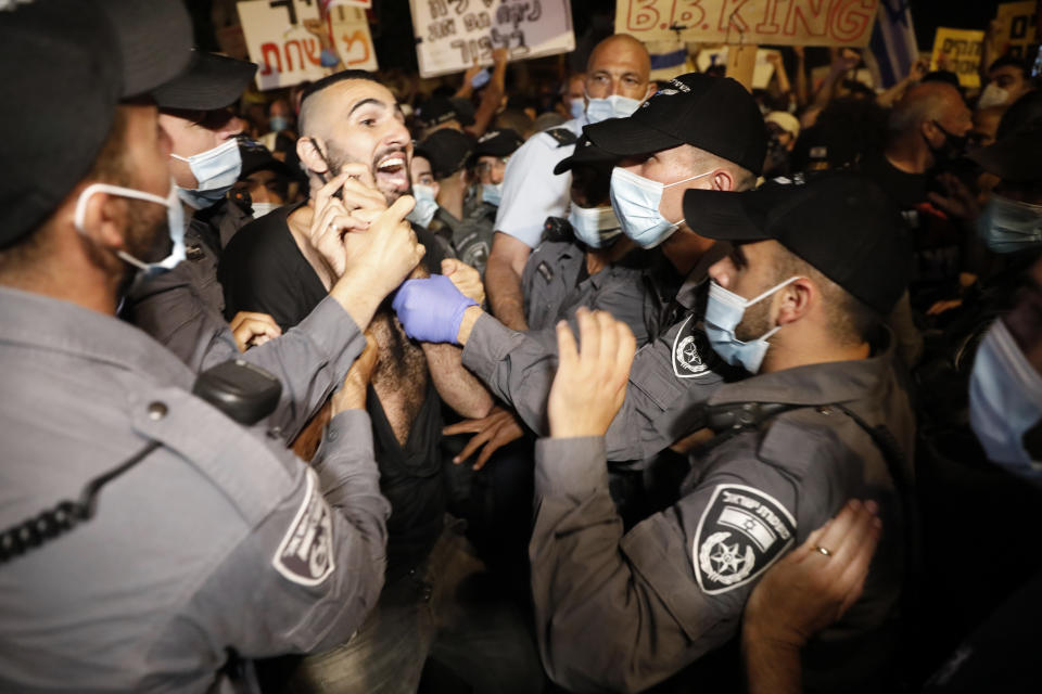 Israeli police officers push a protester outside Prime Minister's residence in Jerusalem, Tuesday, July 14, 2020. Thousands of Israelis on Tuesday demonstrated outside the official residence of Prime Minister Benjamin Netanyahu, calling on the embattled Israeli leader to resign as he faces a trial on corruption charges and grapples with a deepening coronavirus crisis. The signs reads "You are detached. We are fed up".(AP Photo/Ariel Schalit)