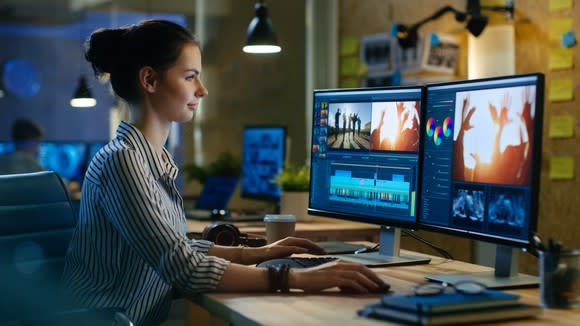 Female video editor working on edits on two monitors in contemporary office.