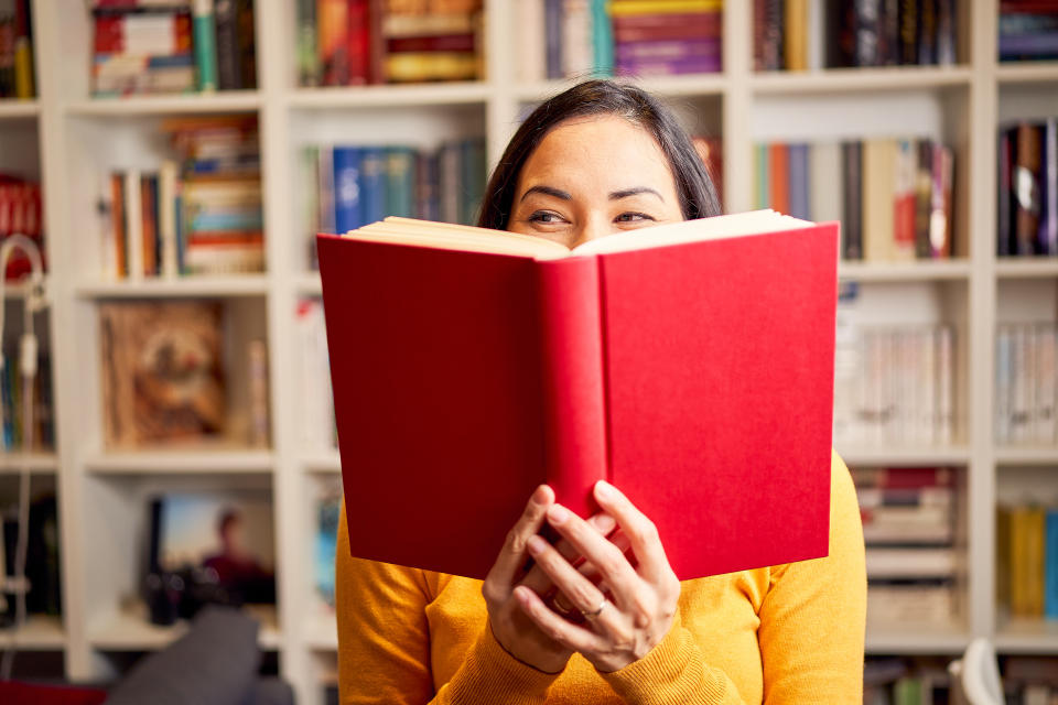 A woman reading a book in front of a tall bookshelf