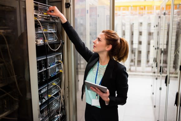 A woman holding a tablet and examining a business server.