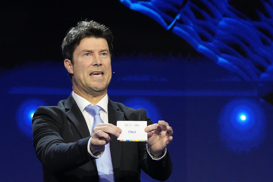 Former soccer player Brian Laudrup holds up the name Italy during the draw for the UEFA Euro 2024 soccer tournament finals in Hamburg, Germany, Saturday, Dec. 2, 2023. (AP Photo/Martin Meissner)